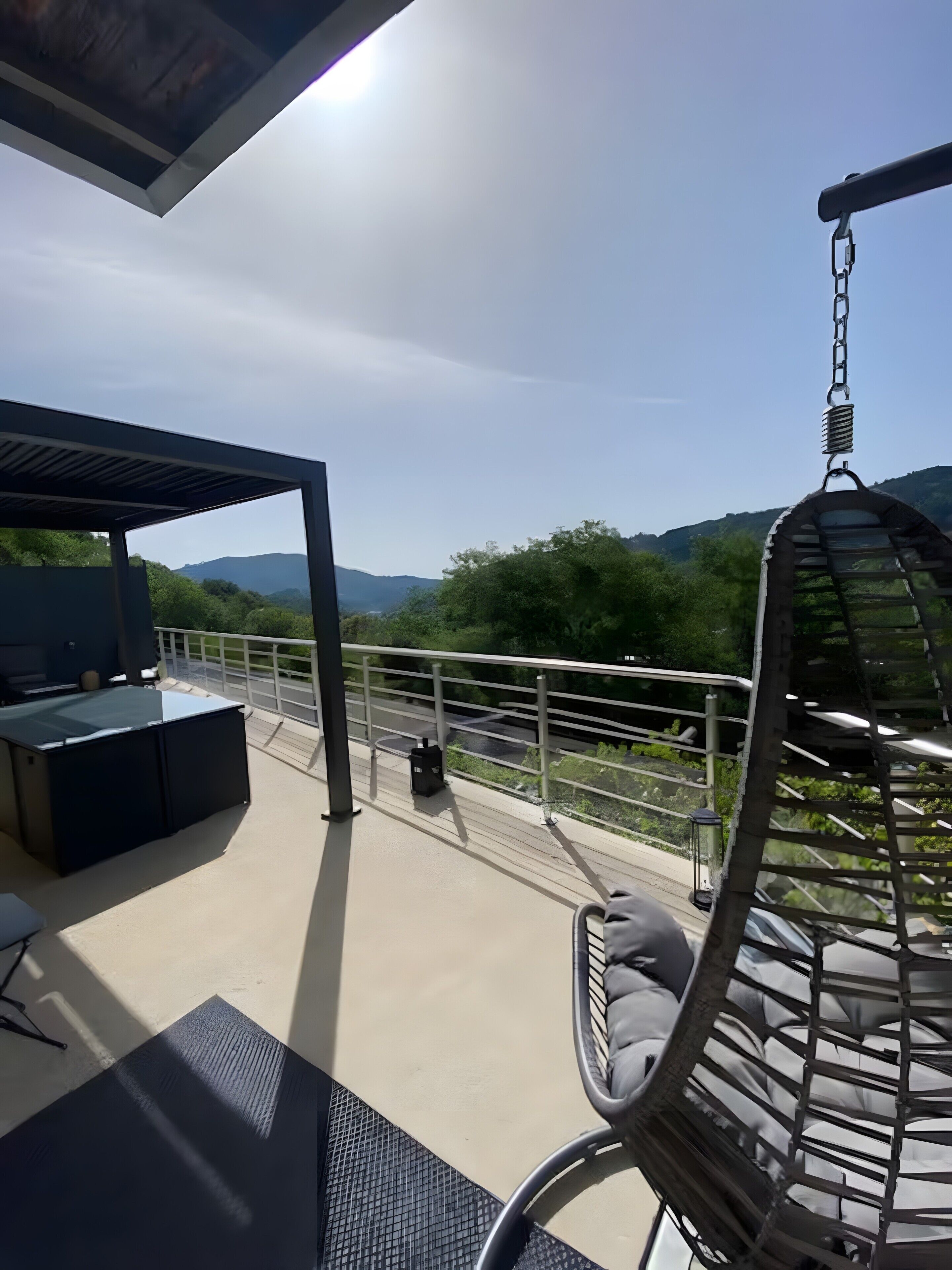 Ein überdachter Außenbereich mit Hängesessel, Grill und Blick auf die umliegende Landschaft.
