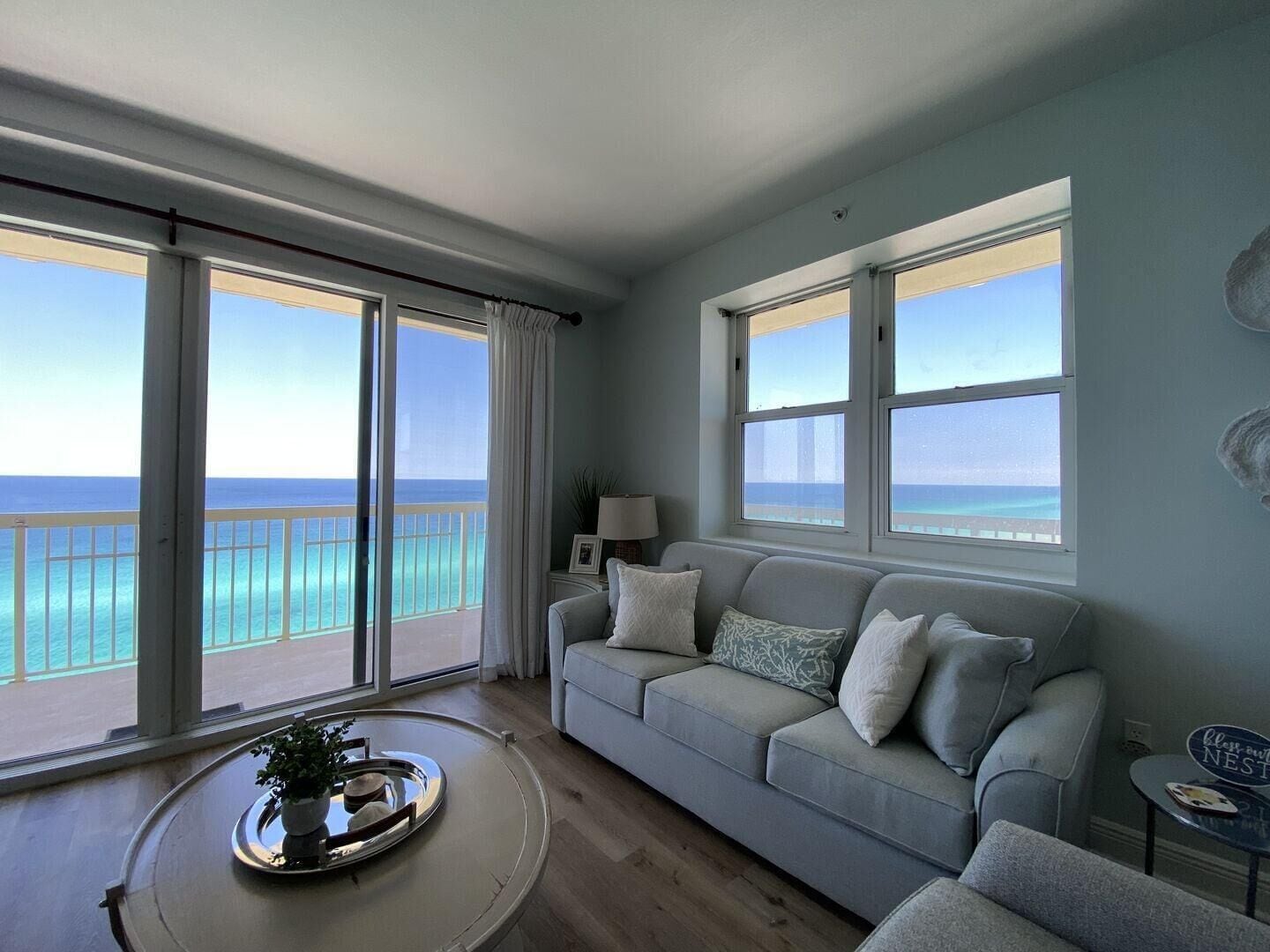 Ein Wohnzimmer mit einer Couch, einem kleinen Tisch mit Tablett und Blick auf den Ozean durch große Fenster.