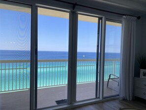 A room with a large sliding glass door leading to a balcony with a view of the ocean and a sailboat. - Celadon 1609a- Waves of Grace (Panama City Beach)