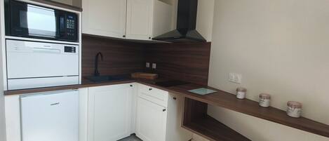 A compact kitchen with white cabinets, a built-in microwave, a black range hood, and a wooden countertop.