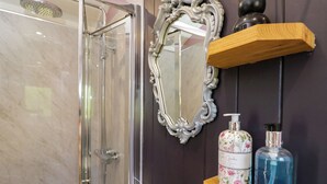 Une salle de bain dotée d’une douche à parois de verre, d’un miroir décoratif et d’étagères où sont rangés les articles de toilette.
