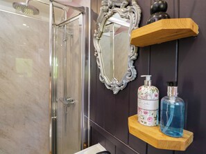 Ein Badezimmer mit einer Duschkabine, einem dekorativen Spiegel und Regalen für Pflegeprodukte.