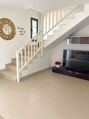 A staircase with white railings leading to a landing, a flat-screen TV on a dark stand, and a decorative mirror on the wall. - BEAUTIFUL DUPLEX WITH A TERRACE IN COSTA TEGUISE (Costa Teguise)