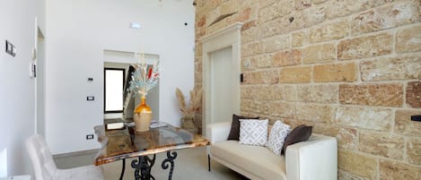 A room with a stone wall, a white sofa, a glass-top table, and a chandelier.