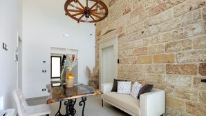 A room with a stone wall, a white sofa, a glass-top table, and a chandelier.