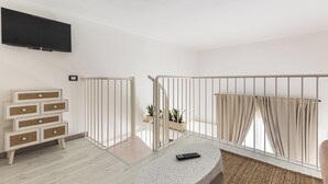 A modern living room with a flat-screen TV mounted on the wall, a white console table with drawers, a round coffee table, and a balcony with a white railing.