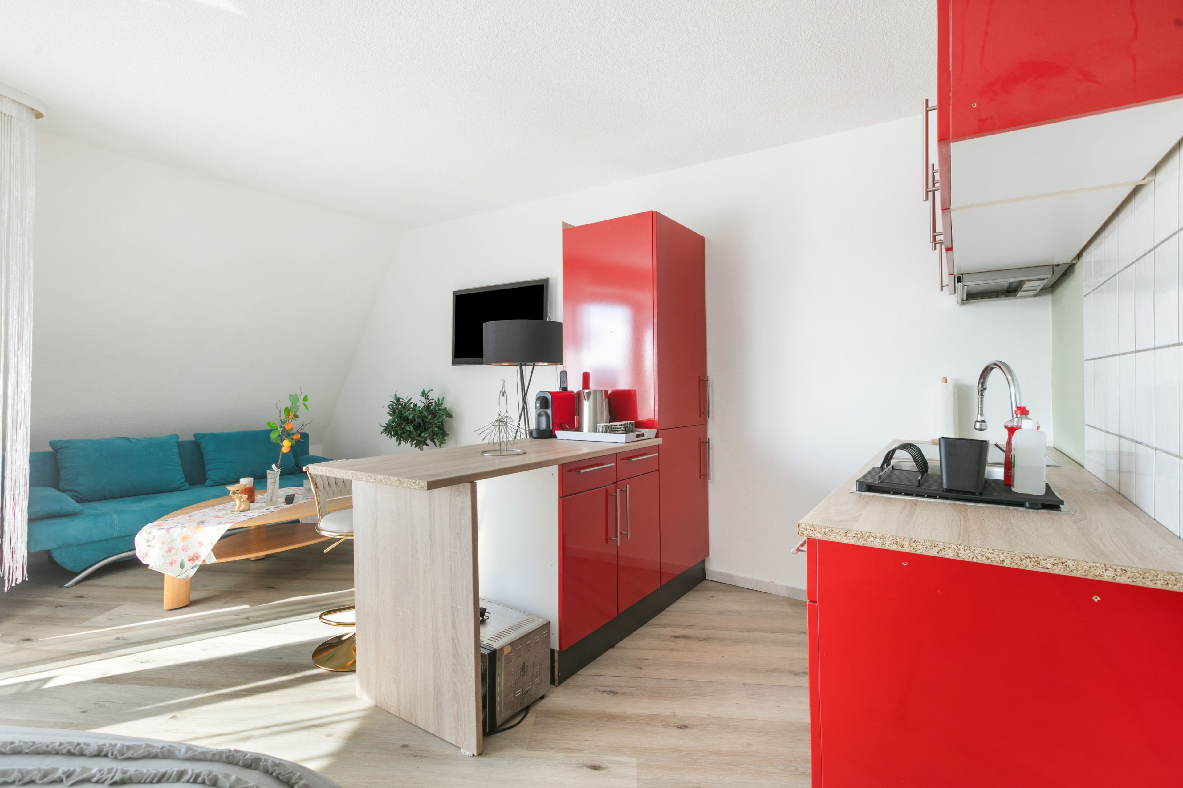 Un espacio habitable compacto con kitchenette, un sofá y un televisor montado en la pared.