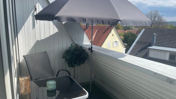 A balcony with a chair, a table, a potted plant, and a large umbrella. - Apartment Domus Lux 406 with Balcony and Wi-Fi (Bad Säckingen)