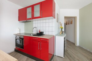 Eine kleine Küche mit roten Schränken, einem weißen Kühlschrank und einer gefliesten Spritzschutzwand.