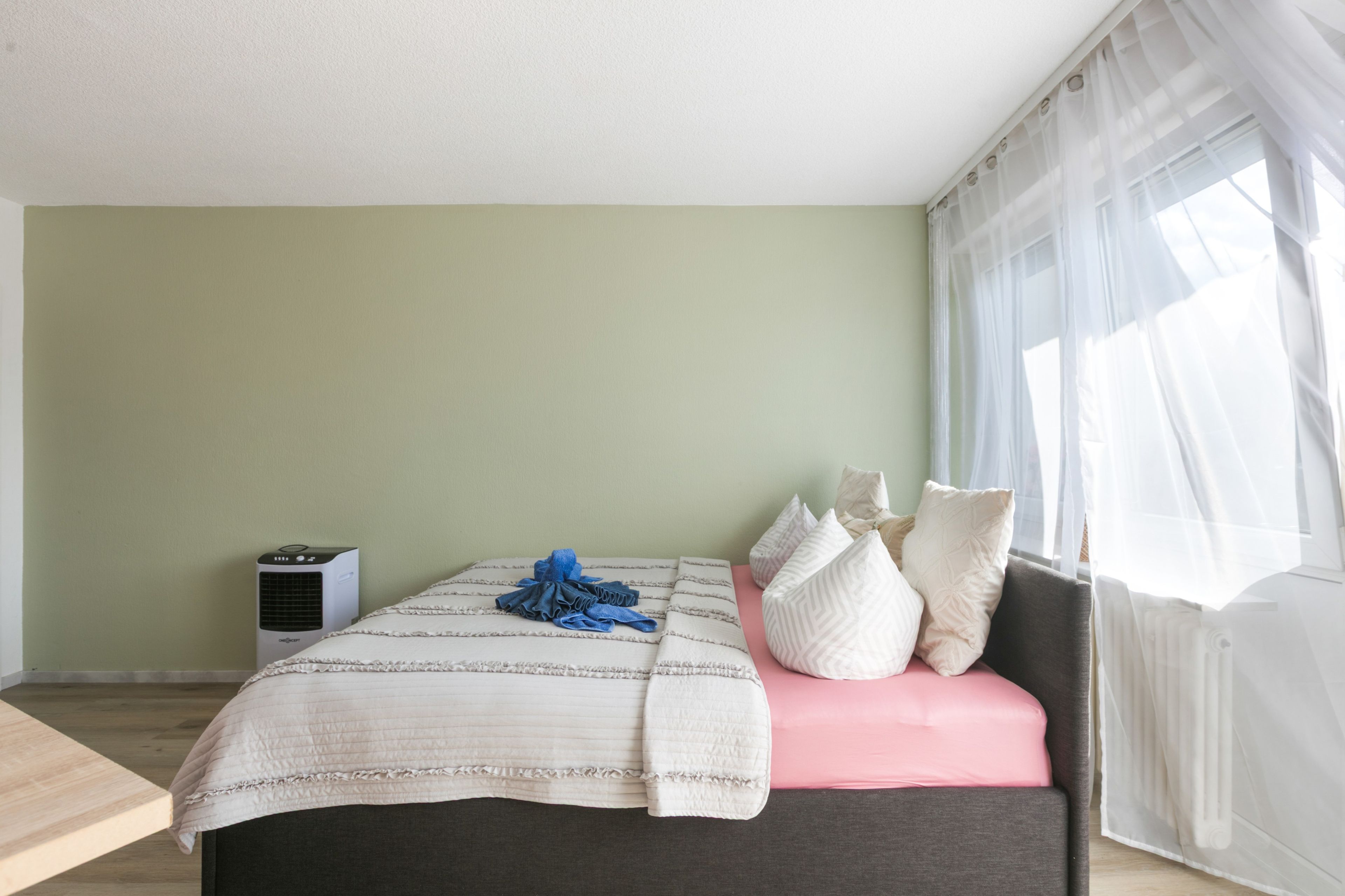 Ein Schlafzimmer mit einem Bett, Kissen, einem Nachttisch und einem Fenster mit Vorhängen.