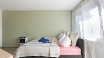 Een slaapkamer met een bed, kussens, een nachtkastje en een raam met gordijnen.