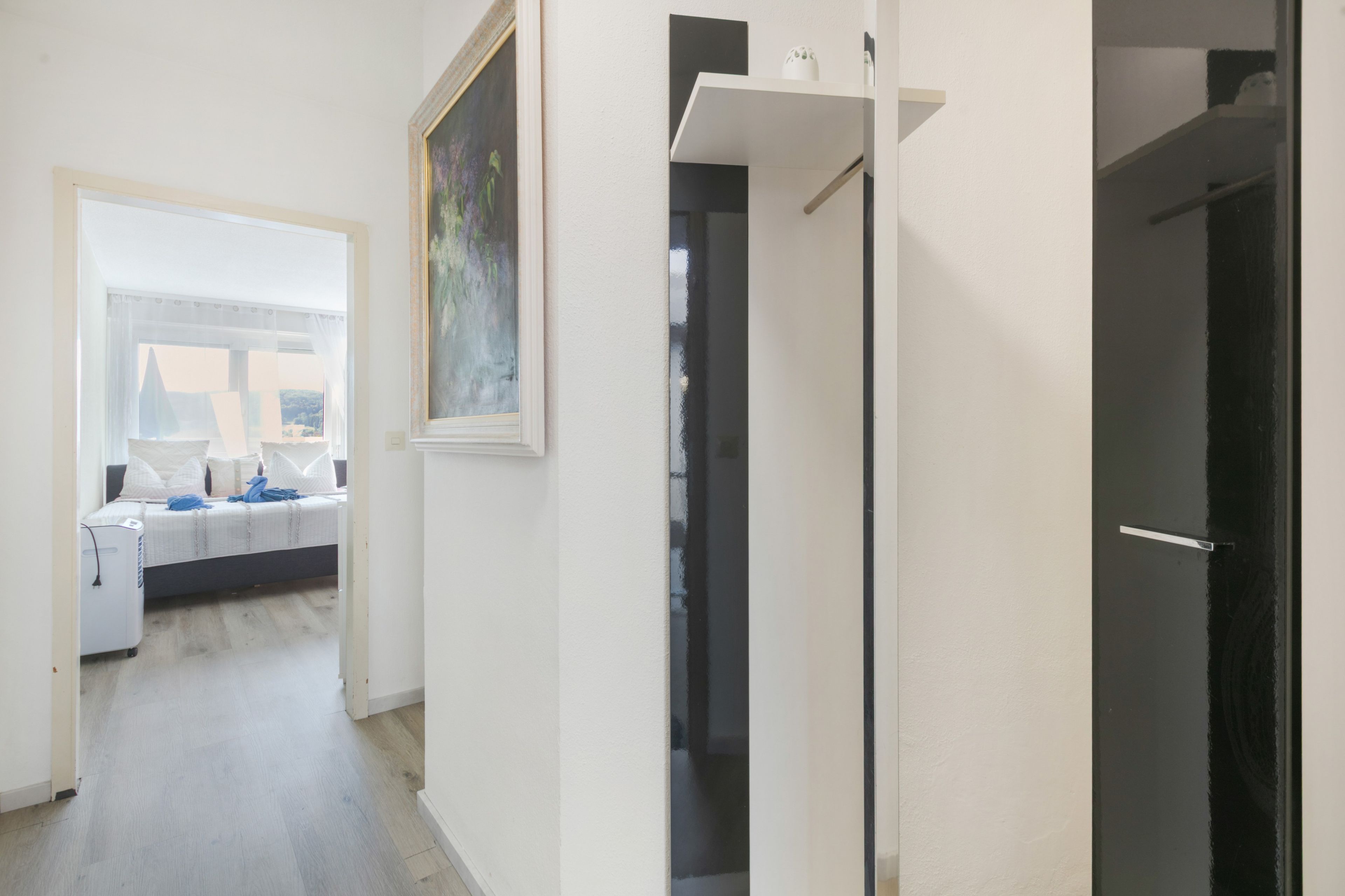 Um corredor com uma cama, um quadro e uma porta.
