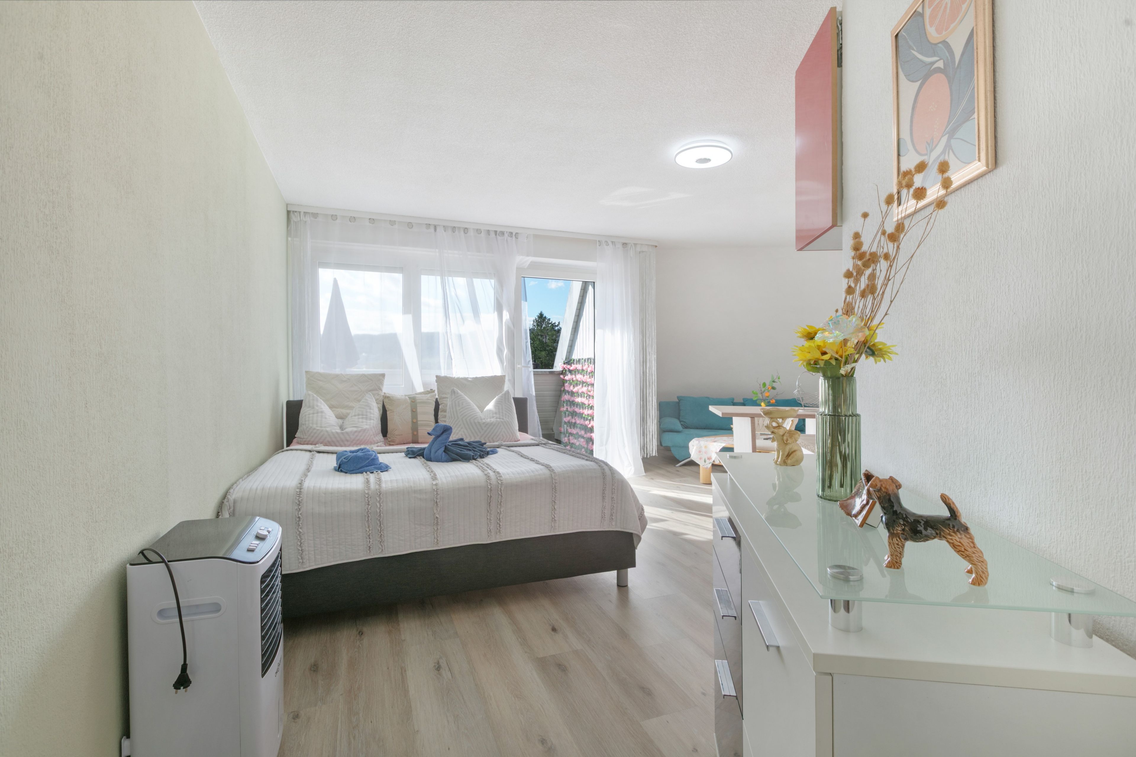 A modern bedroom with a bed, bedside table, and a desk with a vase of flowers.