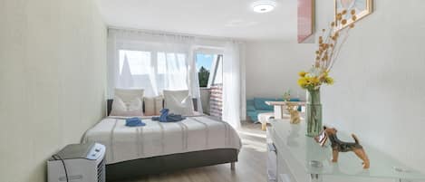 A modern bedroom with a bed, bedside table, and a desk with a vase of flowers.