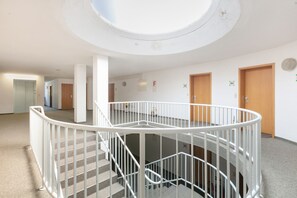 Ein mehrgeschossiges Interieur mit einer zentralen Treppe, weißen Geländern und einem Oberlicht.