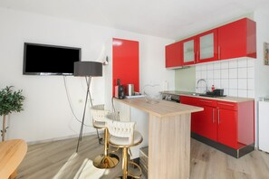 A modern kitchen with red cabinets, a wooden countertop, and a bar area with two white bar stools.
