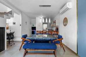 A modern dining area with a glass-top table, blue upholstered chairs, and a wooden bench. - Casa Ivarica Spacious Home for 20 (Mezcales)