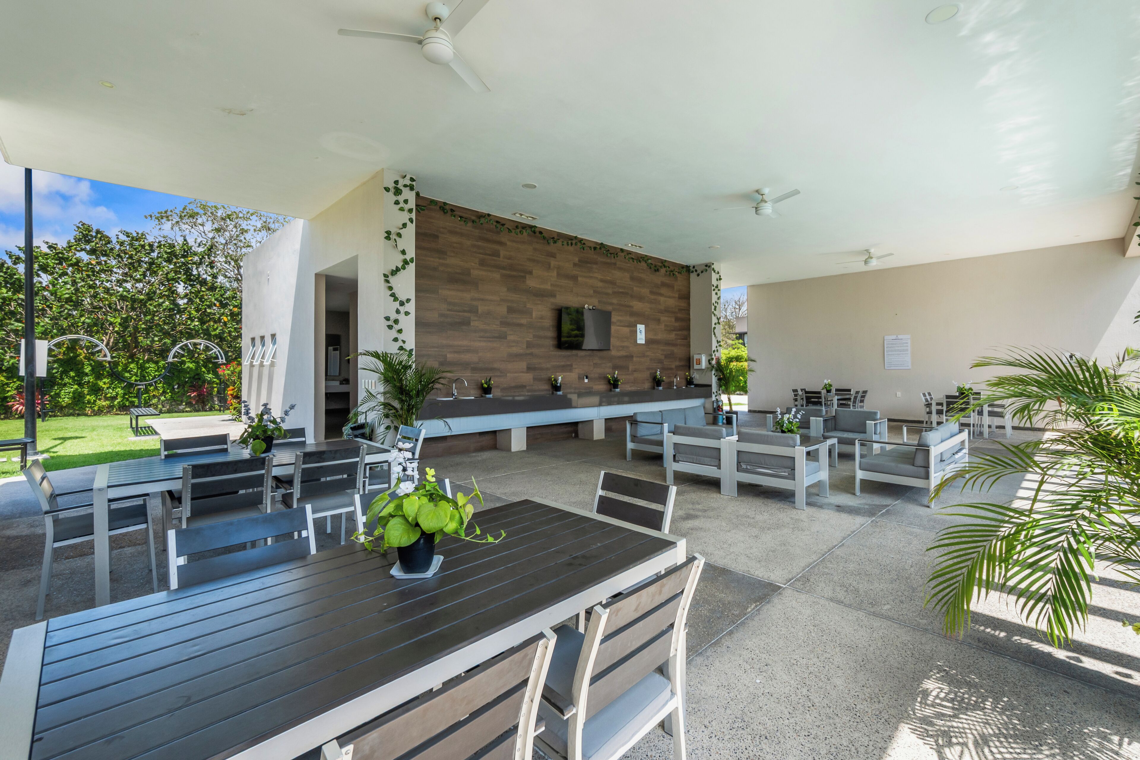 An outdoor seating area with multiple tables and chairs, a wooden wall, and ceiling fans.