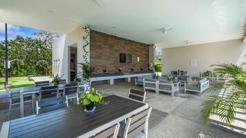 An outdoor seating area with multiple tables and chairs, a wooden wall, and ceiling fans.