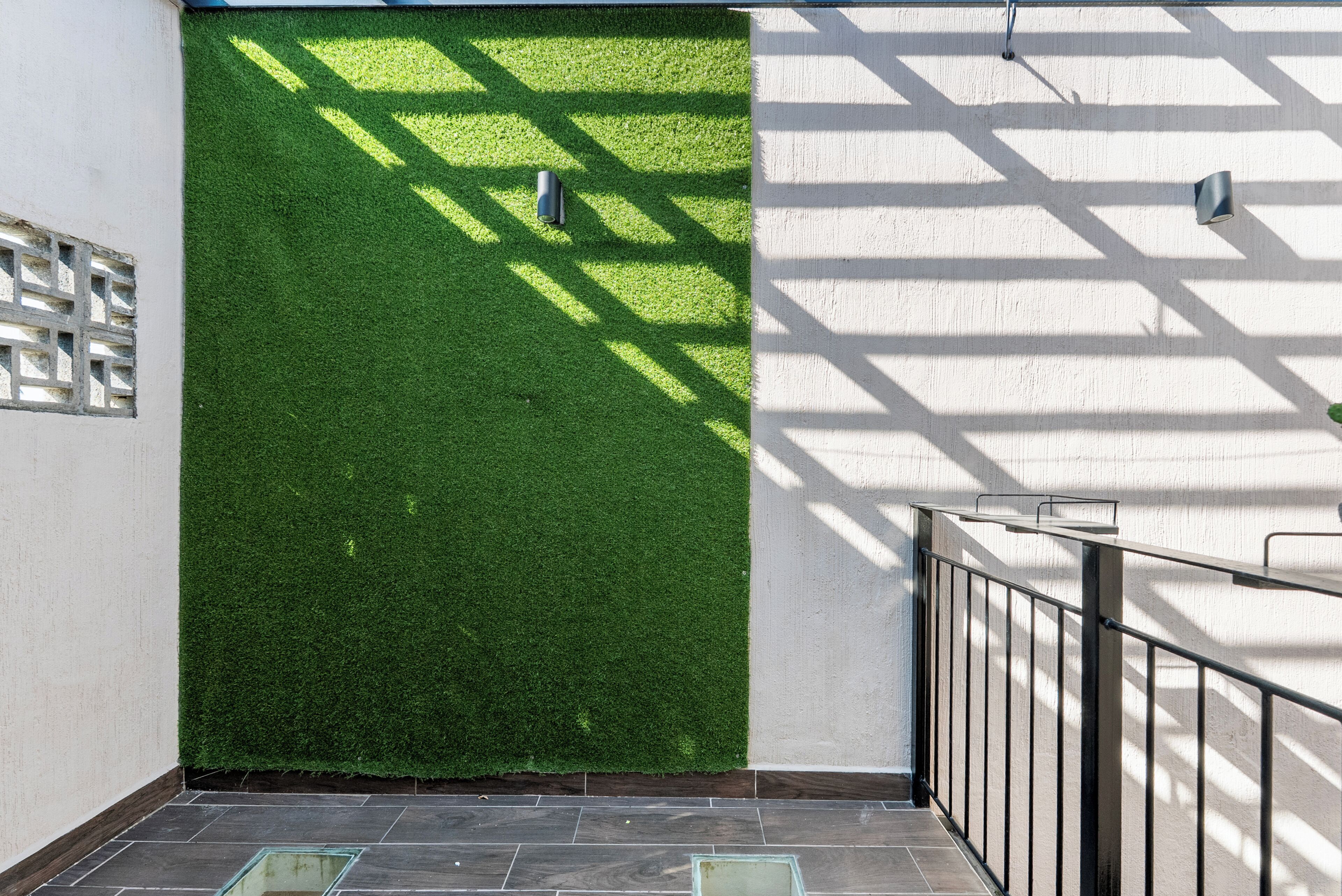 Entrada de un edificio moderno con un muro de césped artificial verde, barandilla metálica y piso de baldosas.