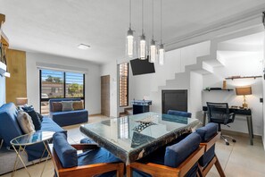 Una sala de estar moderna con una mesa de centro de vidrio, sofás azules y un comedor con un tablero de ajedrez.