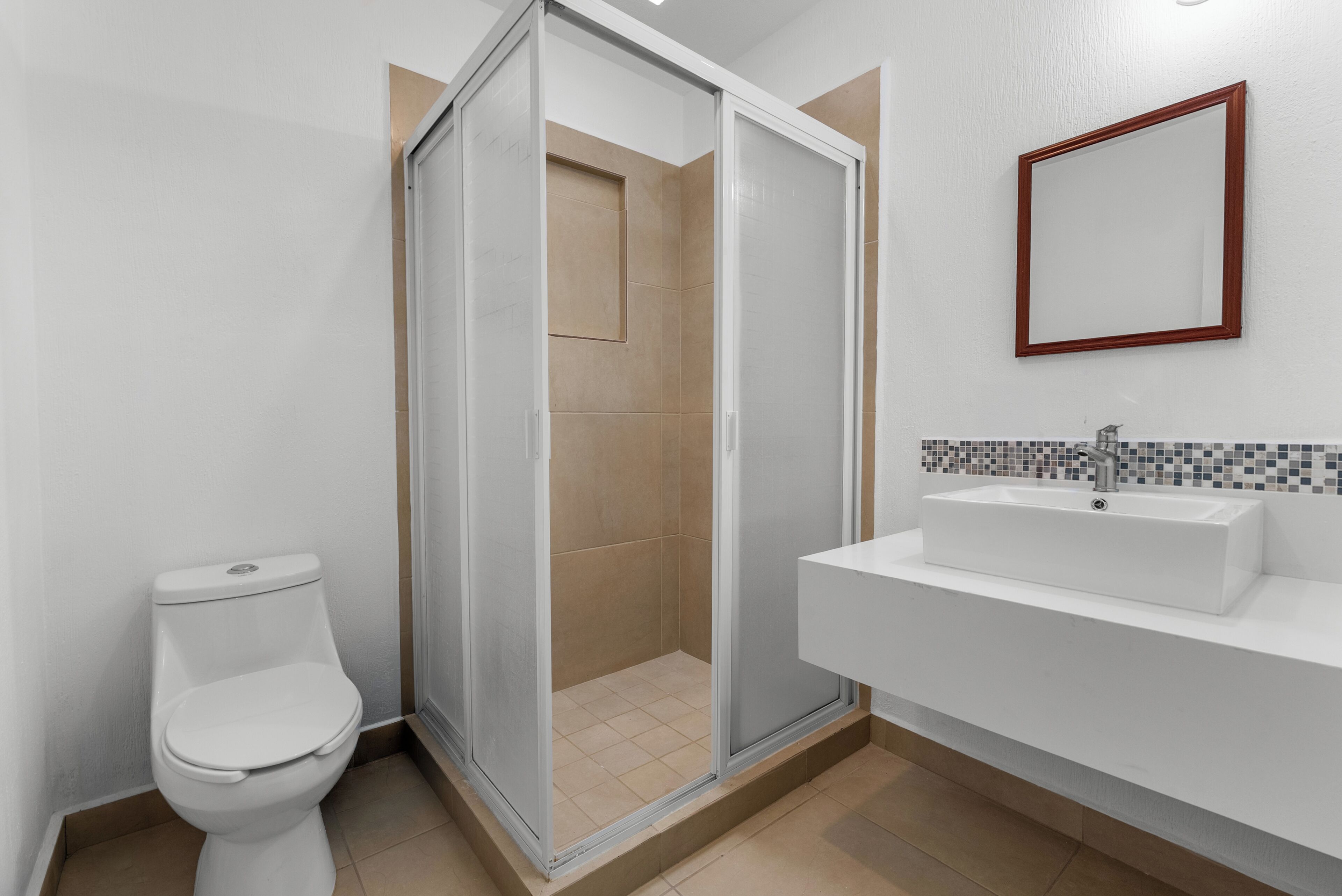 Un baño con inodoro, cabina de ducha y lavamanos con salpicadero de azulejos.