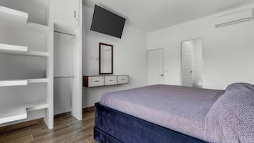 Een slaapkamer met een bed, een kledingkast, een aan de muur bevestigde televisie en een deur die naar een andere kamer leidt.