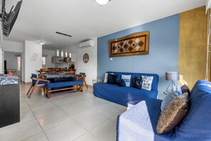A modern living room with a blue sofa, a dining area with a glass table, and a kitchen in the background. - Casa Ivarica Spacious Home for 20 (Mezcales)