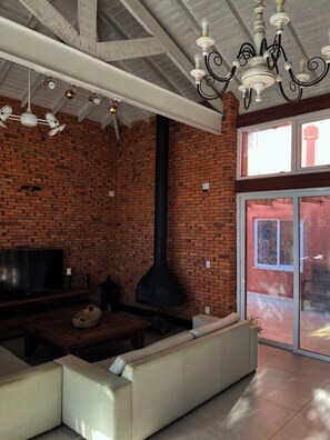Una habitación con pared de ladrillo, chimenea negra, sofá blanco, televisor y candelabro.