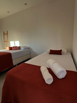 A hotel room with two beds, each with a red blanket and pillows, and a pair of rolled towels on the bed.
