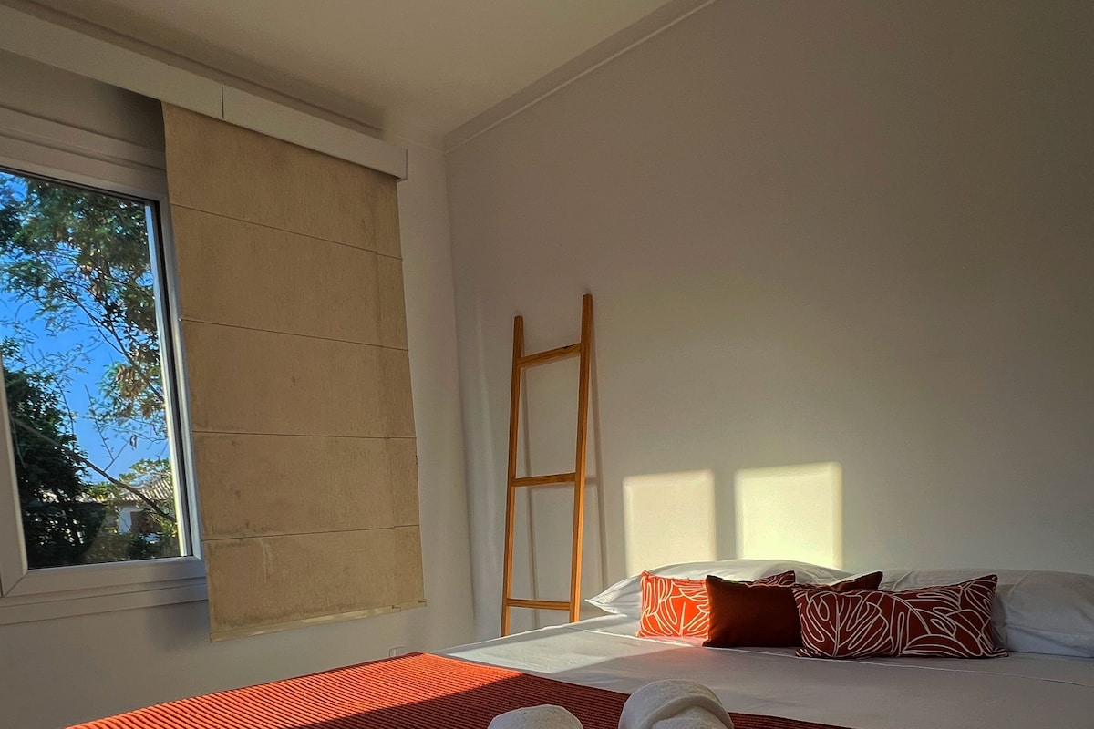 A bedroom with a large bed, a window, and a wooden ladder.