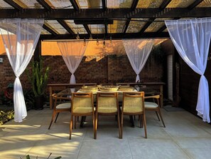 Un patio exterior con una mesa y sillas, un muro de ladrillo y una pérgola con techo de malla.
