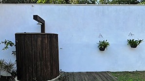 A rustic wooden water feature with a metal spout, surrounded by a wooden deck and potted plants against a white wall.