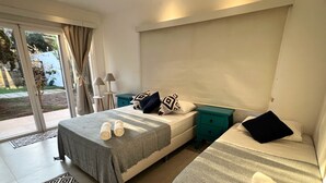 A hotel room with two beds, a sliding glass door to the outside, a small table with a lamp, and a patterned rug.