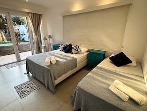 A hotel room with two beds, a sliding glass door to the outside, a small table with a lamp, and a patterned rug.