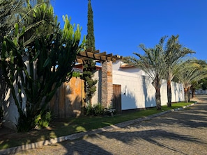 Un edificio con fachada de piedra, una pérgola de madera y un camino adoquinado.