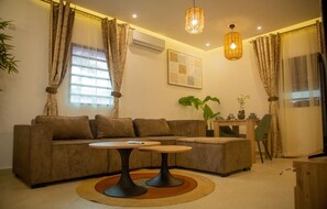 A living room with a sofa, two small tables, a plant, and a TV stand. - Cozy 1-bedroom apartment in Abidjan with AC (Abidjan)