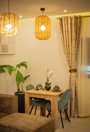 A dining area with a wooden table, chairs, a potted plant, and hanging lamps. - Cozy 1-bedroom apartment in Abidjan with AC (Abidjan)