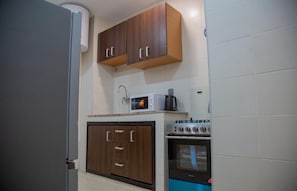 A kitchen with wooden cabinets, a microwave, a coffee maker, and an oven. - Cozy 1-bedroom apartment in Abidjan with AC (Abidjan)