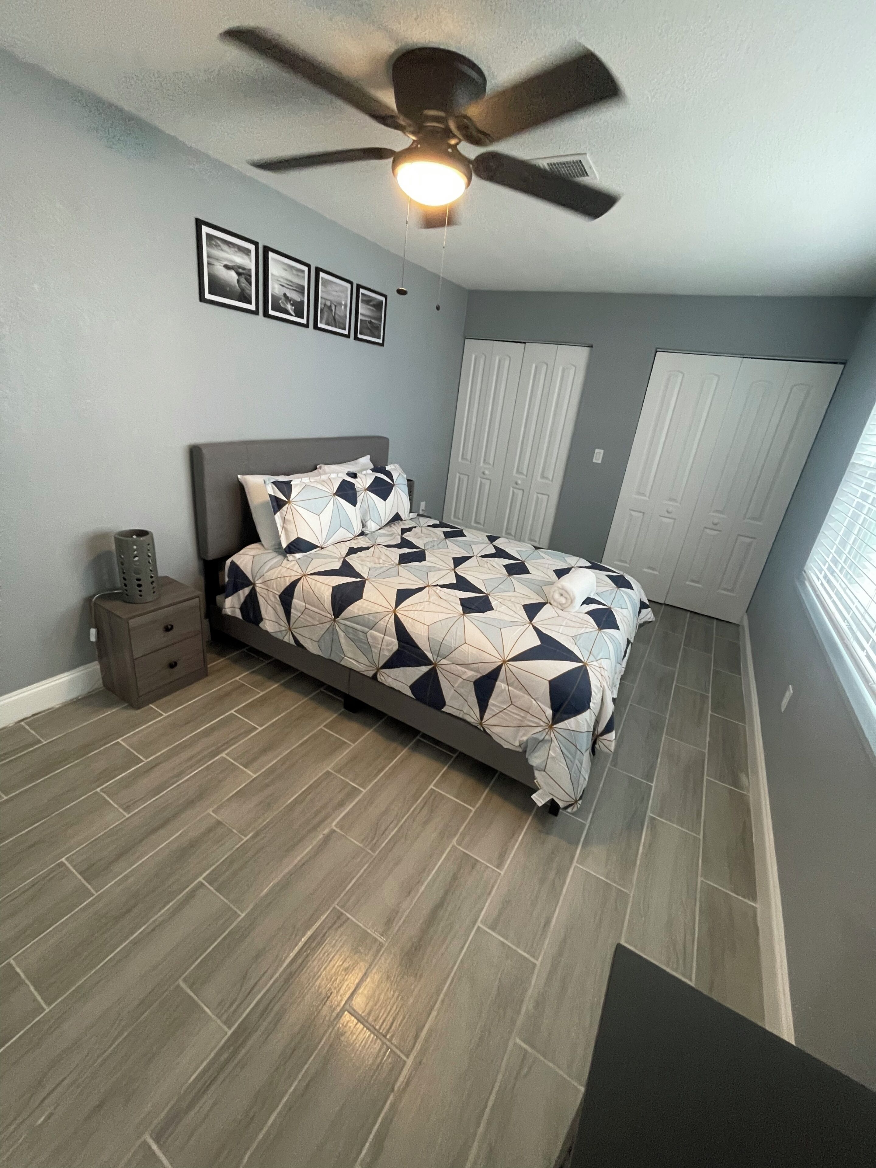 A bedroom with a bed, a ceiling fan, a nightstand, and a wardrobe.