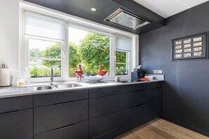 A modern kitchen with a large window, a built-in stove, and a black wall with a framed picture. - 3 bedroom accommodation in Sint Idesbald (Sint Idesbald)