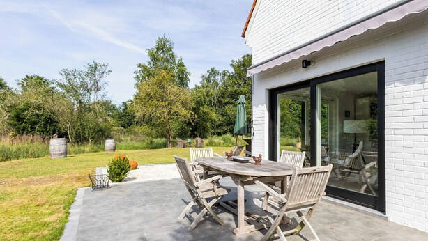 A patio with a wooden table and chairs, a green umbrella, and a white brick building with a glass door. - 3 bedroom accommodation in Sint Idesbald (Sint Idesbald)
