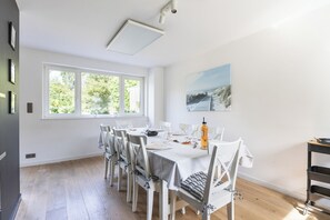 Uma sala de jantar com mesa posta para seis pessoas, cadeiras brancas e um quadro na parede.