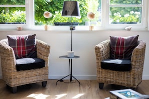 Two wicker chairs with plaid cushions, a small round table with a lamp, and a view of greenery through a window. - 3 bedroom accommodation in Sint Idesbald (Sint Idesbald)
