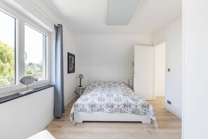Um quarto com uma cama, uma janela com cortinas, um abajur e uma porta.