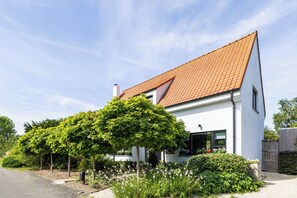 A white two-story house with a red-tiled roof, surrounded by lush greenery and a gravel driveway. - 3 bedroom accommodation in Sint Idesbald (Sint Idesbald)