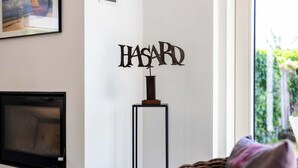A room with a mounted artwork spelling 'HASARD' on a wall, a television on the left, and a wicker chair with a cushion. - 3 bedroom accommodation in Sint Idesbald (Sint Idesbald)
