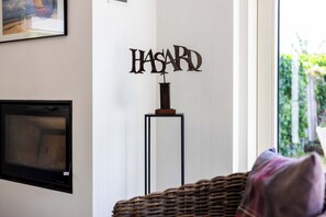 A room with a mounted artwork spelling 'HASARD' on a wall, a television on the left, and a wicker chair with a cushion. - 3 bedroom accommodation in Sint Idesbald (Sint Idesbald)