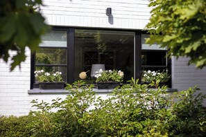 A white building with a window featuring two flower boxes with white flowers and a bird feeder. - 3 bedroom accommodation in Sint Idesbald (Sint Idesbald)