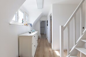 Un couloir étroit avec une commode blanche, un miroir et un escalier.